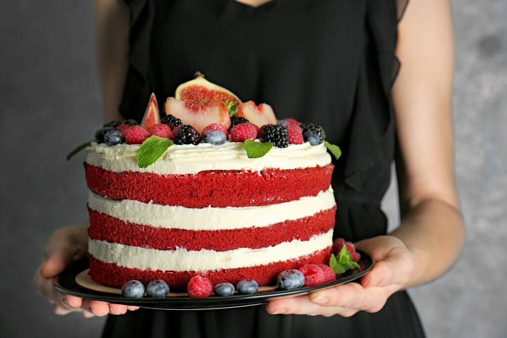 Red velvet cake with berrys and figs on top. Cake is carried by a person wearing a black dress.