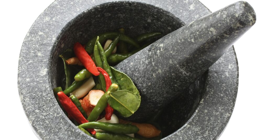 A stone mortar and pestle with Thai chilies and spices
