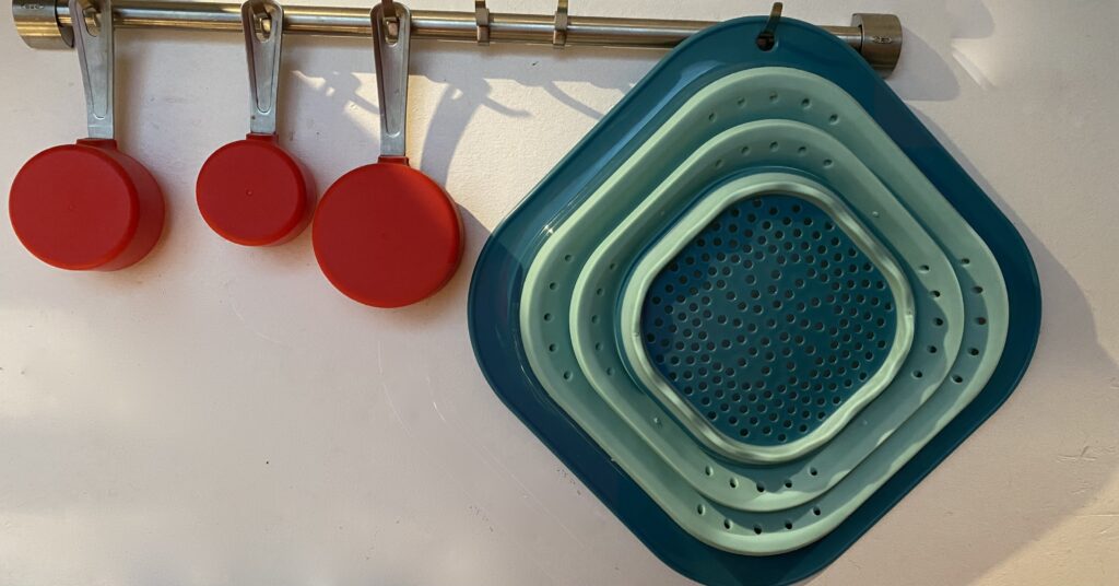 collapsible colander on a hook with red measuring cups