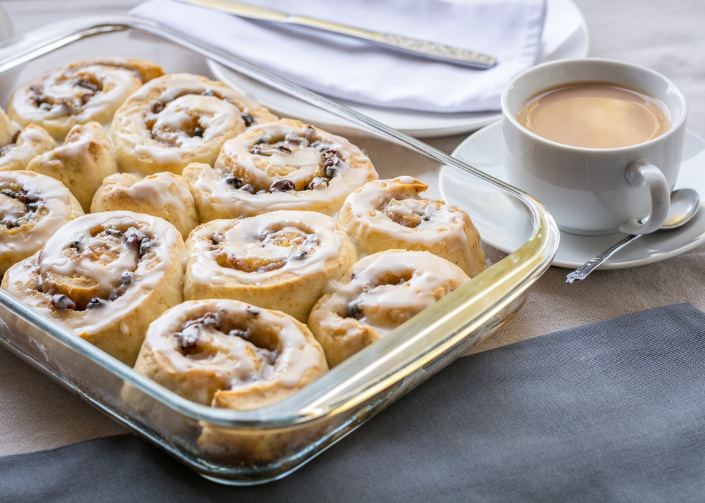 Pyrex Baking Dish with cinnamon buns on top of a wooden cutting board with a cup of coffee next to it.